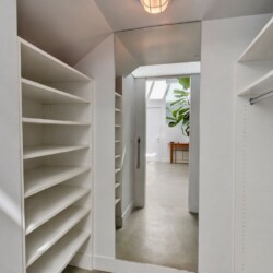 Walk-in closet with white built-in shelves and a full-length mirror reflecting a bright room with a potted plant.