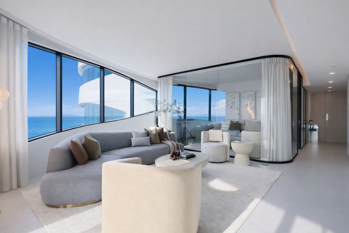 Bright, modern living room with curved floor-to-ceiling windows showing a blue ocean view and white architectural curves outside.