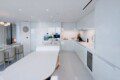 Bright white kitchen with glossy cabinets, an oval island, and built-in double ovens in the background.