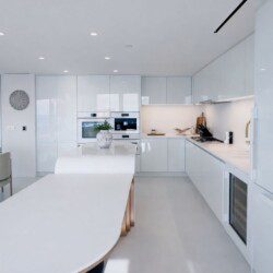 Bright white kitchen with glossy cabinets, an oval island, and built-in double ovens in the background.
