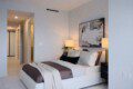 Modern bedroom with a white upholstered bed, taupe bedding, and a framed abstract black‑and‑white artwork above the headboard.
