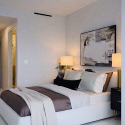 Modern bedroom with a white upholstered bed, taupe bedding, and a framed abstract black‑and‑white artwork above the headboard.