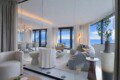 Bright open-concept living room with floor-to-ceiling windows and an ocean view, neutral sofas, round coffee tables, and soft beige decor.