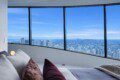 Modern bedroom with a curved wall of floor-to-ceiling windows overlooking a clear blue city skyline.