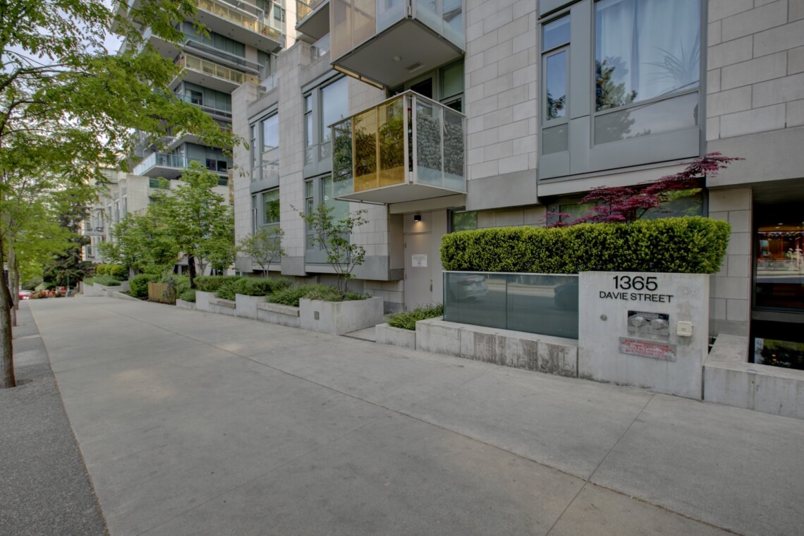 Modern residential building with glass balconies along a tree-lined street; sign reads 1365 Davie Street in front.