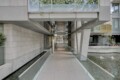 Modern concrete building entrance with glass railings and a water-filled canal on both sides, leading to glass doors at the center.