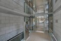 Modern building entrance with large glass doors, gray brick walls, and a stainless steel security kiosk near the door.