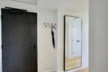 Interior hallway with a dark front door on the left, wooden coat hooks and an umbrella, and a tall framed mirror reflecting a white door.