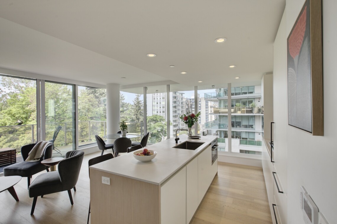 Bright open-concept kitchen and living area with large floor-to-ceiling windows and cityscape views behind a modern island.