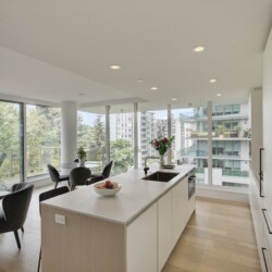 Bright open-concept kitchen and living area with large floor-to-ceiling windows and cityscape views behind a modern island.