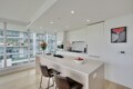 Bright, modern kitchen with white cabinets, an island, and large windows overlooking an urban cityscape with balconies and glass buildings.