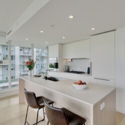 Bright, modern kitchen with white cabinets, an island, and large windows overlooking an urban cityscape with balconies and glass buildings.