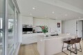 Bright modern kitchen with white cabinetry, a large island, and city view through floor-to-ceiling windows on the left.