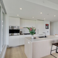 Bright modern kitchen with white cabinetry, a large island, and city view through floor-to-ceiling windows on the left.
