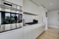 Modern white kitchen with stainless steel wall ovens, gas cooktop, and a hexagonal tiled backsplash between white cabinets.