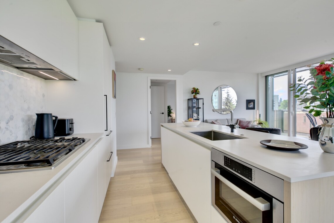 Bright, modern kitchen with a long white island, stainless oven and gas range, and white cabinetry along the left wall.