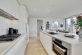 Bright, modern kitchen with a long white island, stainless oven and gas range, and white cabinetry along the left wall.