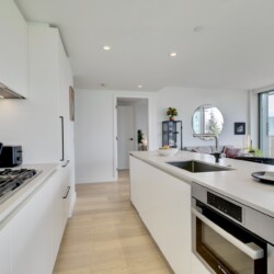 Bright, modern kitchen with a long white island, stainless oven and gas range, and white cabinetry along the left wall.