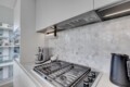 Modern kitchen with a gas range, stainless vent hood, and hexagonal marble backsplash; windowed city view in the background.