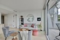 Bright modern living room with a gray sofa and pink cushions, circular wall mirror, and glass sliding doors to a balcony.