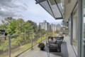 Balcony seating with two black wire chairs and a small table, glass railing, overlooking trees and city buildings in the distance.