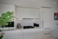 Modern white kitchen with upper cabinets, a hexagonal tile backsplash, and small appliances on the counter (plant in foreground).