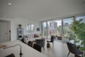 Bright living room with white walls, gray sofa, round mirror, and glass doors to a balcony overlooking the city.