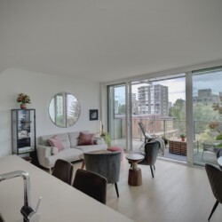Bright living room with white walls, gray sofa, round mirror, and glass doors to a balcony overlooking the city.