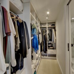 Walk-in closet with organized racks of shirts, jackets, and shelves, adjacent to a glass-enclosed marble bathroom shower.