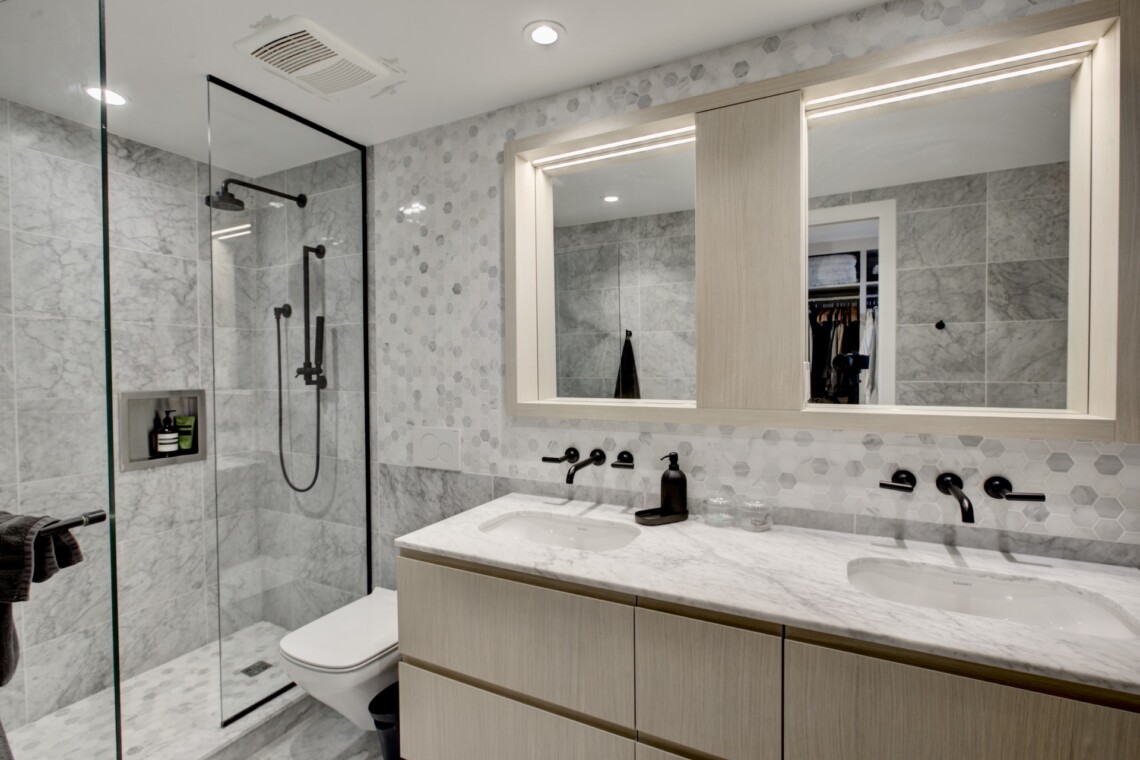 Modern bathroom featuring a glass shower enclosure, marble walls, and a light wood vanity with a marble countertop.