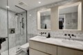 Modern bathroom featuring a glass shower enclosure, marble walls, and a light wood vanity with a marble countertop.