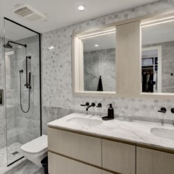 Modern bathroom featuring a glass shower enclosure, marble walls, and a light wood vanity with a marble countertop.