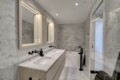 Modern bathroom with a marble double vanity, hex tile backsplash, and a glass shower door in a bright space.