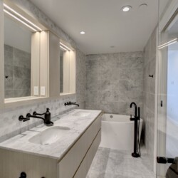 Modern bathroom with a marble double vanity, hex tile backsplash, and a glass shower door in a bright space.
