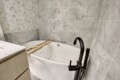 Bathtub with a wooden bath rack inside a marble-tiled bathroom, curved black faucet visible to the right.