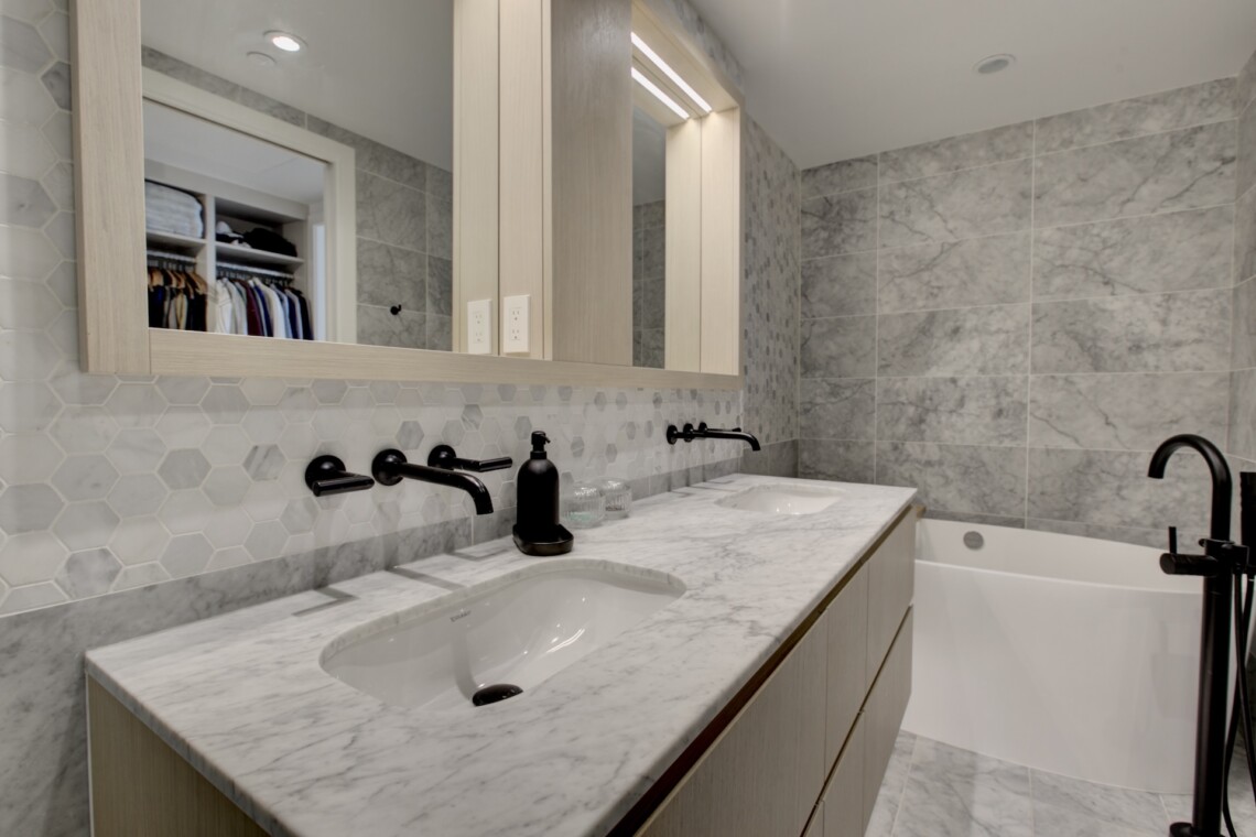 Modern bathroom with a marble countertop double sink, hex tile backsplash, and black fixtures.