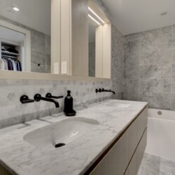 Modern bathroom with a marble countertop double sink, hex tile backsplash, and black fixtures.