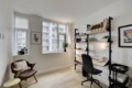 Bright home office with large windows, white walls, and a black metal shelving unit filled with books and folders.