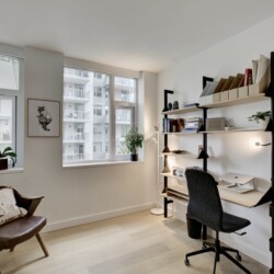 Bright home office with large windows, white walls, and a black metal shelving unit filled with books and folders.