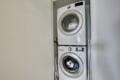 Stacked white front-loading washer and dryer in a narrow laundry closet with doors open to the side.