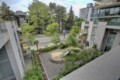 Bird's-eye view of a modern apartment courtyard with trees, greenery, and a circular seating area with a slide nearby on paved surfaces.