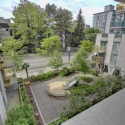 Bird's-eye view of a modern apartment courtyard with trees, greenery, and a circular seating area with a slide nearby on paved surfaces.