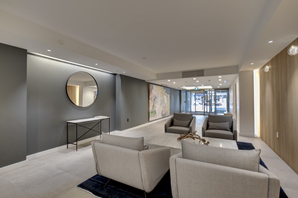 Modern hotel lobby with gray walls, circular wall mirror, and gray seating area facing a mural.