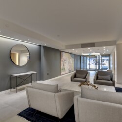Modern hotel lobby with gray walls, circular wall mirror, and gray seating area facing a mural.