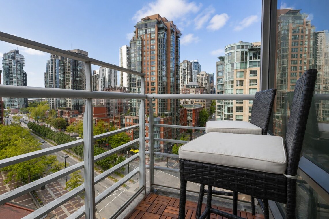 Balcony with two wicker chairs and cream cushions overlooking a cityscape of modern high-rise buildings.