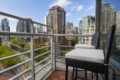 Balcony with two wicker chairs and cream cushions overlooking a cityscape of modern high-rise buildings.