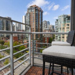 Balcony with two wicker chairs and cream cushions overlooking a cityscape of modern high-rise buildings.