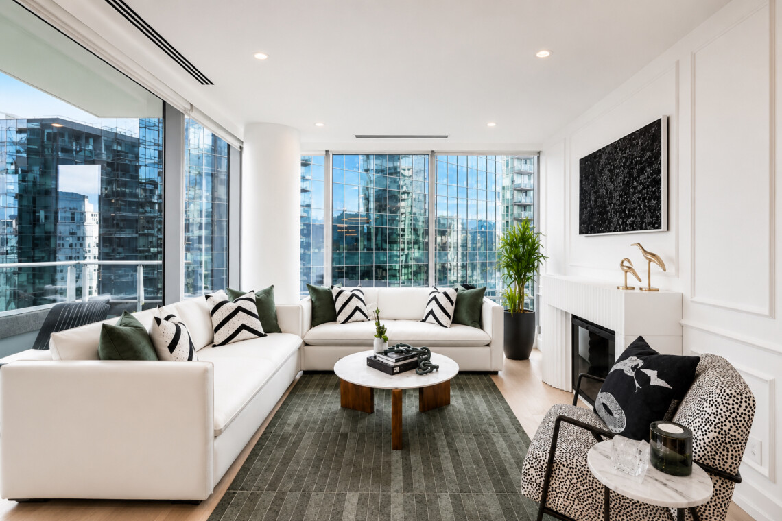 Bright modern living room with a white sectional, green and black-and-white cushions, and floor-to-ceiling city-view windows.