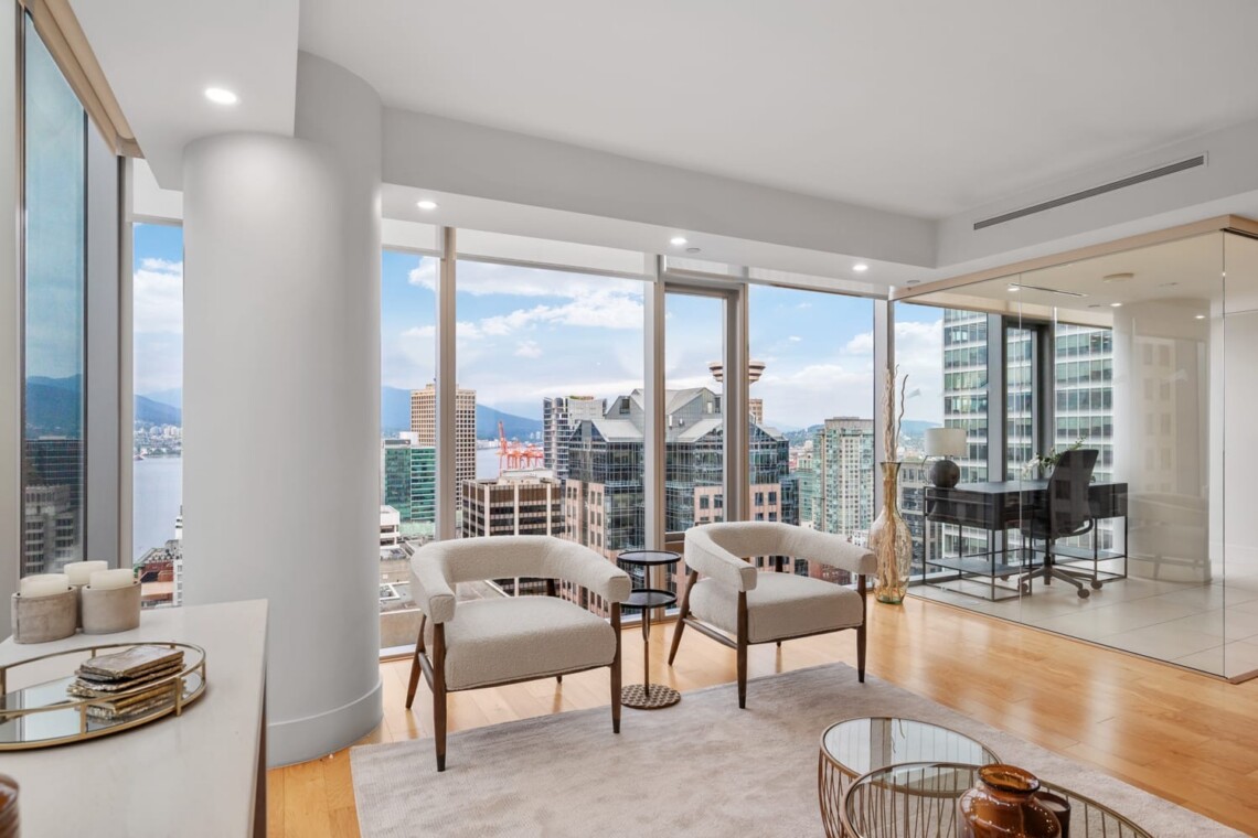 Contemporary lounge with two beige armchairs facing a city skyline through floor-to-ceiling windows.