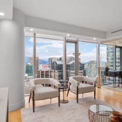 Contemporary lounge with two beige armchairs facing a city skyline through floor-to-ceiling windows.